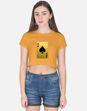 Woman wearing a mustard yellow crop top with a playing card design and blue denim shorts on a white background
