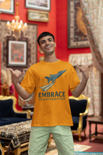 Man wearing a yellow t-shirt with a rocket graphic and 'Embrace Transformation' text in a decorated room.