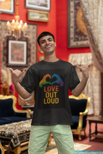 Man wearing a black t-shirt with 'Love Out Loud' design in a decorated room.