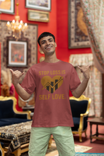 Man wearing a t-shirt with 'Stop Loss is Self Love' text in a decorated room.