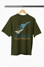 Green t-shirt with airplane graphic and 'Embrace Transformation' text on a hanger.