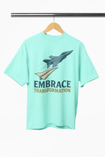 Mint green t-shirt with airplane graphic and 'Embrace Transformation' text on a hanger.
