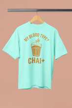Mint green t-shirt with 'My Blood Type? Chai+' text on a hanger against a beige background