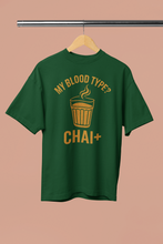 Green t-shirt with yellow text 'My Blood Type? CHAI+' on a hanger against a beige background