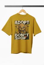 Mustard yellow t-shirt with a dog graphic and 'Adopt Don't Shop' text on a hanger.