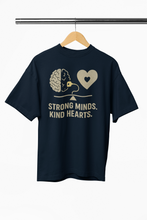 Navy blue t-shirt with graphic design and text 'Strong Minds, Kind Hearts' on a hanger against a white background.