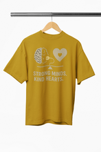 Yellow t-shirt with 'Strong Minds. Kind Hearts.' text and graphic on a hanger against a white background