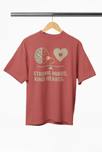 Red t-shirt with 'Strong Minds. Kind Hearts.' text and graphics on a hanger against a white background