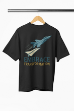 Black t-shirt with airplane graphic and 'Embrace Transformation' text on a hanger against a white background