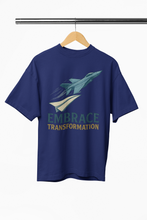 Blue t-shirt with airplane graphic and 'Embrace Transformation' text on a hanger.