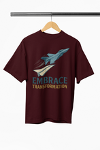 Maroon t-shirt with airplane graphic and 'Embrace Transformation' text on a hanger.