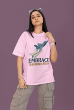 Person wearing a pink t-shirt with a graphic and text 'Embrace Transformation' on a purple background