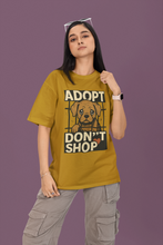 Person wearing a mustard yellow t-shirt with an 'Adopt Don't Shop' graphic on a purple background